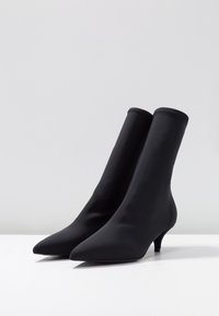 Černé kotníkové boty s elegantním, špičatým designem, vyrobené z hladkého materiálu, s nízkým podpatkem a bezproblémovou konstrukcí.