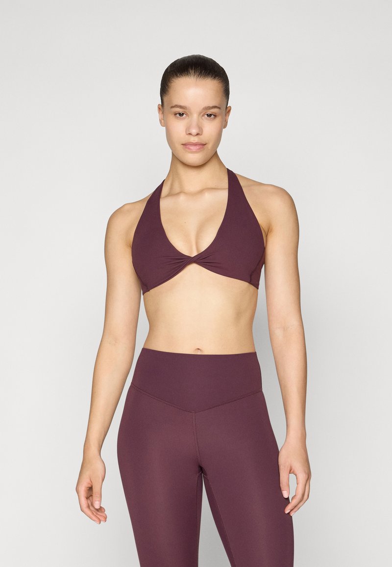 Burgundy sports bra with a plunging neckline and twist detail; paired with high-waisted, seamless leggings in matching color.