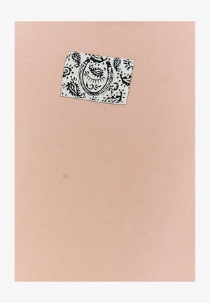 Jasnoróżowa tkanina z małą białą prostokątną naszywką z czarnymi abstrakcyjnymi wzorami oka i podkowy.