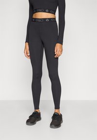 Leggings en coton noir avec une coupe ajustée, dotés d'une large ceinture ornée d'un logo texturé. Associés à des chaussures de sport noires.