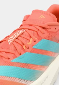 Biegowy but Adidas Adizero w kolorze koralowym i turkusowym z siateczkową cholewką, koralowymi sznurowadłami i widocznym logo na języku oraz bocznych paskach.