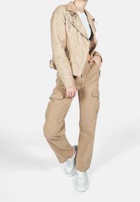 Béžová kožená motorkářská bunda se zipovými kapsami, spárovaná s khaki cargo kalhotami se bočními kapsami. Pohodlné bílé tenisky dotvářejí vzhled.