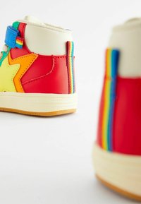 Rote und gelbe High-Top Sneaker mit einem Sternendesign, ausgestattet mit einem blauen Klettverschlussband und Regenbogenakzenten an der Ferse und Seite.