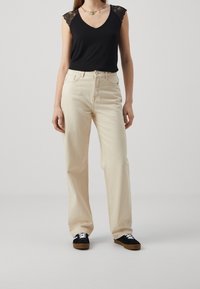 Sort ærmeløs top med blonde detaljer, lyse beige vidde bukser og sorte sneakers med hvide snørebånd og brune såler.