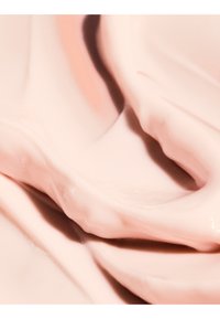 Hellrosa Creme mit glatter und glänzender Textur, die weiche Falten und sanfte wellenartige Muster aufweist.