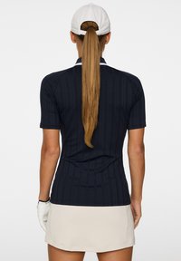 Polo shirt golf a righe navy con maniche corte, abbinato a una gonna beige. Un cappellino bianco completa il look sportivo.