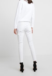 Jeans skinny de mezcla de algodón blanca con una cintura a media altura, bolsillos traseros y dobladillo deshilachado, combinados con sandalias negras de tacón.