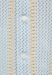 Lichtblauw gebreid shirt met crèmekleurige textuurstrepen en een decoratieve knoop aan de voorkant.