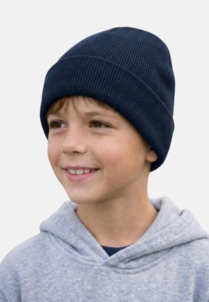 Smiling young boy wearing a navy blue knit beanie and light gray hoodie, looking slightly to the right on a neutral background.