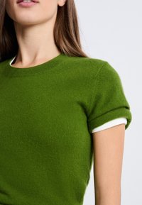 Zielony sweter z krótkim rękawem wykonany z miękkiej tkaniny, z okrągłym dekoltem i białymi podwiniętymi mankietami dla kontrastu.