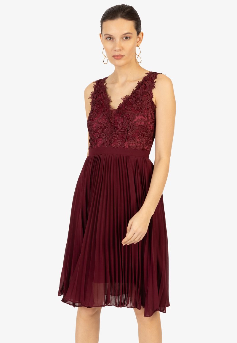 Robe bordeaux avec un corsage brodé, dotée d'un décolleté en V et d'une jupe plissée. Le matériau semble léger et fluide.