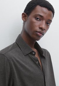 Dark gray, collared shirt featuring a button placket, short sleeves, and a soft texture. Fit appears relaxed with smooth fabric draping.