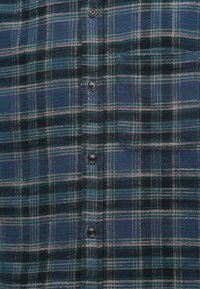 Καρό φλοράλ πουκάμισο σε σκούρο πράσινο, μπλε και μαύρο. Διαθέτει κουμπιά και απαλή υφή με οριζόντιες και κάθετες γραμμές.