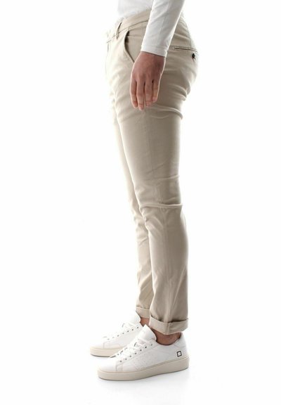 Pantaloni beige slim fit con una texture liscia, vita media e tasche, abbinati a sneaker bianche con dettagli perforati e lacci.