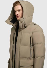 Parka beige isolata con un ampio cappuccio, zip frontale e tasche laterali. Presenta accenti neri e una finitura testurizzata.