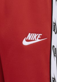 Pantaloni sportivi rossi realizzati in tessuto liscio, con un logo Nike bianco e un nastro brandizzato in bianco e nero lungo il lato.