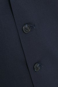 Tumši zils audums ar teksturētu virsmu, kreisajā pusē divas apaļas pelēkas pogas un dekoratīva šuvuma apdare.