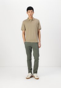Beżowa koszulka polo z krótkim rękawem, zestawiona z oliwkowymi spodniami slim fit i białymi sneakersami z brązowymi podeszwami. Prosty design i neutralne kolory.