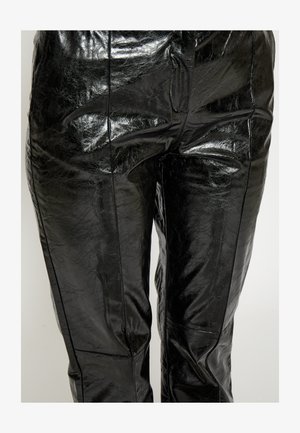 Melnas ādas bikses ar spīdīgu, struktūru virsmu. Tās ietver sānu šuves un piegulošu siluetu, izceļot modernu dizainu.