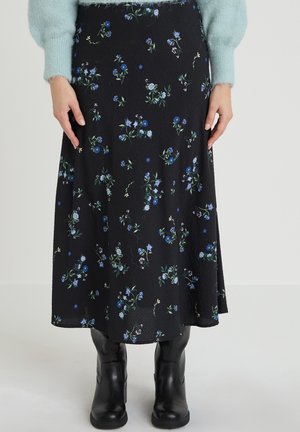 Jupe midi noire à petit imprimé floral bleu et blanc, portée avec un pull duveteux bleu clair et des bottines en cuir noir.