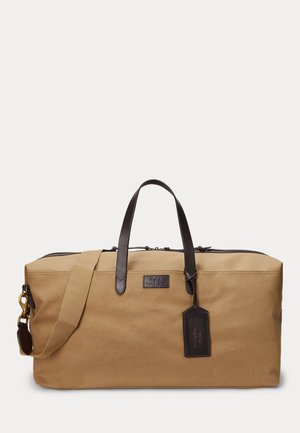 Borsa da viaggio in tela color cammello con dettagli in pelle marrone scuro, doppie maniglie, tracolla staccabile e un'etichetta in pelle attaccata.
