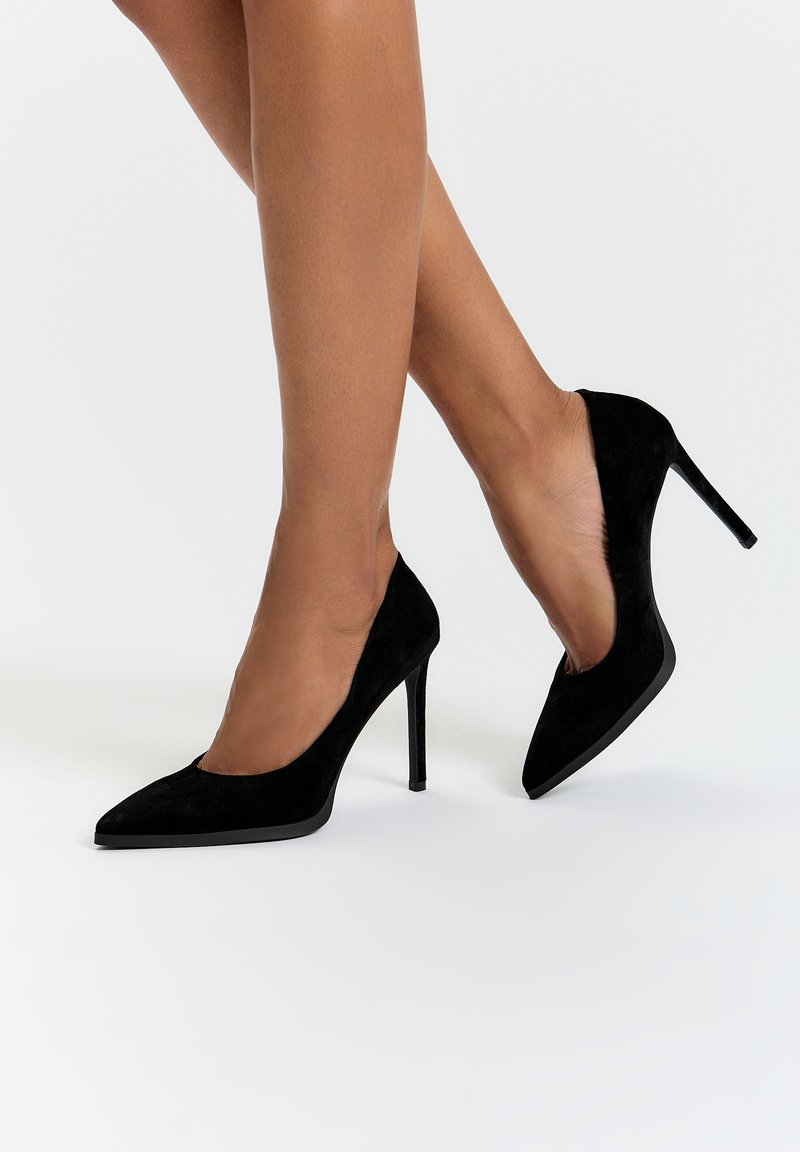 Musta mokkanahka korkeakorkoiset kengät, joissa on teräväkärkinen muotoilu ja 10 cm:n stiletto-korko, sisältäen sileän pinnan ja minimalistisen muotoilun.