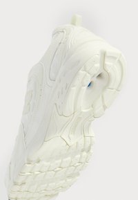 White athletic shoes with a breathable mesh upper, textured toe, and pronounced sole featuring a zigzag tread pattern and blue accent.