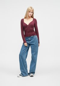 Burgundy long-sleeve top with a wrap design and square neckline, paired with loose-fitting blue jeans and black-and-white sneakers.
