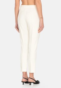 Pantaloni bianchi su misura con una vestibilità slim e una texture liscia. Presentano una vita a media altezza. Abbinati a scarpe slingback nere.
