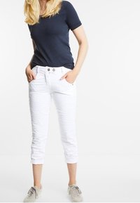 Marineblauw T-shirt met korte mouwen gecombineerd met witte cropped broek met een gestructureerde stof en een sluiting met twee knopen. Grijze sneakers maken de look compleet.