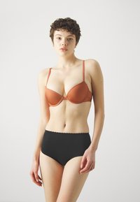 Brown padded bra with adjustable straps and a smooth texture, paired with high-waisted black underwear featuring a scalloped edge.