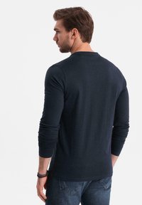 T-shirt a manica lunga navy con scollo a girocollo, vestibilità slim e polsini a costine, abbinato a jeans scuri, visto da dietro.