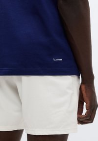 Μπλε σκούρο πουκάμισο ClimaCool με λεία υφή, σε συνδυασμό με λευκό σορτς που έχει διακριτικό σχέδιο πλέγματος. Εστίαση στις λεπτομέρειες του ενδύματος, χωρίς ορατά λογότυπα.