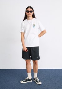Hvit kortermet t-skjorte med fargerik grafikk, svarte treningsshorts, hvite ankelsokker, svarte joggesko og solbriller.