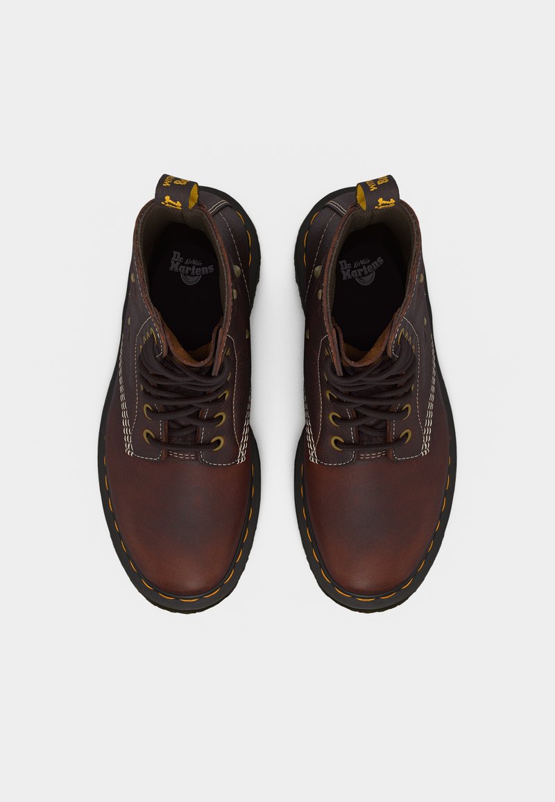 Braune Leder-Schnürstiefel mit gelber Naht, schwarzen Sohlen und gebrandeten Zuganhängern, von oben auf weißem Hintergrund gezeigt.