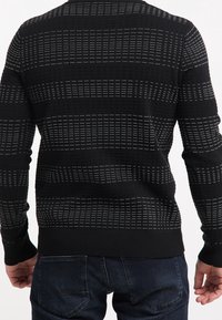 Maglione nero con un motivo a maglia testurizzato che presenta linee verticali e orizzontali. Maniche e orlo aderenti, con una texture a coste nella parte inferiore.
