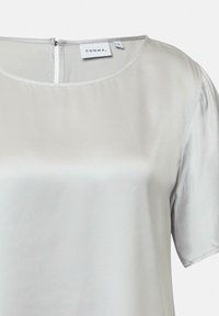 Hellgraue Bluse mit weicher, glatter Textur, rundem Halsausschnitt und kurzen Ärmeln. Sie hat einen Reißverschlussverschluss am Rücken und ein Etikett der Marke.