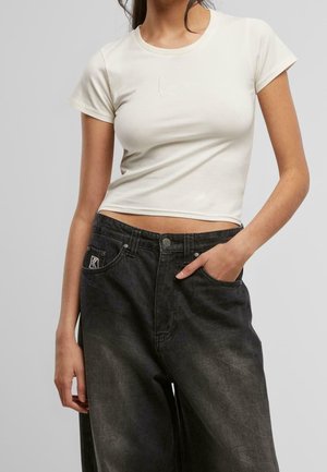 Biała, dopasowana bawełniana koszulka z okrągłym dekoltem i krótkimi rękawami, ozdobiona subtelnym haftowanym logo. Połączona z luźnymi, ciemnymi dżinsami.
