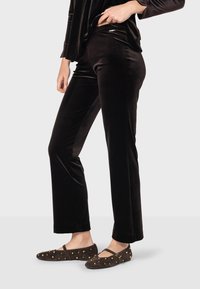 Čierne sametové nohavice s úzkym strihom, ktoré majú hladkú textúru a jemný lesk. Spárované s tmavohnedými semišovými balerínami so zlatými nitmi.