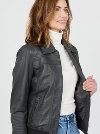 Grå läderjacka med dragkedja fram, ribbade ärmar och krage. Har en sidoficka och slät textur, bärs över en vit turtleneck.