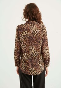 Bluse med leopardprint, lange ærmer, blødt stof og en rund kant. Brun, beige og sorte farver skaber et iøjnefaldende, mønstret design.