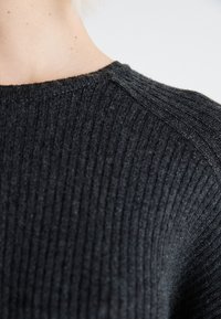 Pull en tricot côtelé gris foncé avec un col rond, une texture subtile et un gros plan sur le détail de la couture de l'épaule.