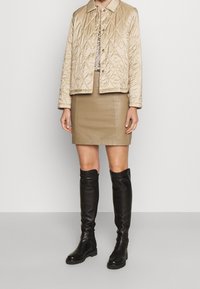 Beige quilted jacket with a collar and snap buttons, paired with a fitted beige leather skirt and knee-high black leather boots.
