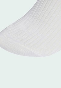 Bílé žebrované ponožky s hladkou texturou a vyztuženou špičkou. Materiál je lehký a pružný, přičemž má jemné vertikální pruhy.