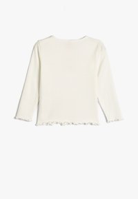 Top à manches longues blanc avec une texture côtelée et un ourlet festonné. Design simple avec un col rond, adapté à un usage décontracté.