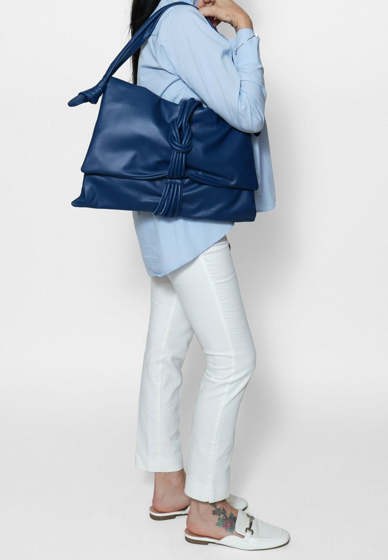 Blauwe leren tote bag met een geknoopte accent, zachte textuur en ruim ontwerp. De tas heeft een schouderband van gemiddelde lengte.