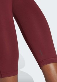 Bordowe legginsy sportowe o gładkiej fakturze i dopasowanym kroju. Posiadają branding AEROREADY w pobliżu dołu oraz kontrastowe szwy.