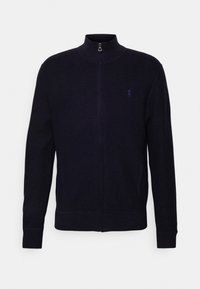 Laivastonsininen vetoketjullinen takki, jossa on korkea kaulus, resorit hihansuissa ja helmassa; rinnassa pieni kontrastivärinen logo. Valmistettu teksturoidusta neulemateriaalista.