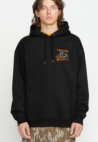 Czarna bluza z kapturem, z przednią kieszenią, z pomarańczowym napisem "VOLCOM" i graficznym logo. Miękka tkanina, długie rękawy i kaptur ze sznurkiem.