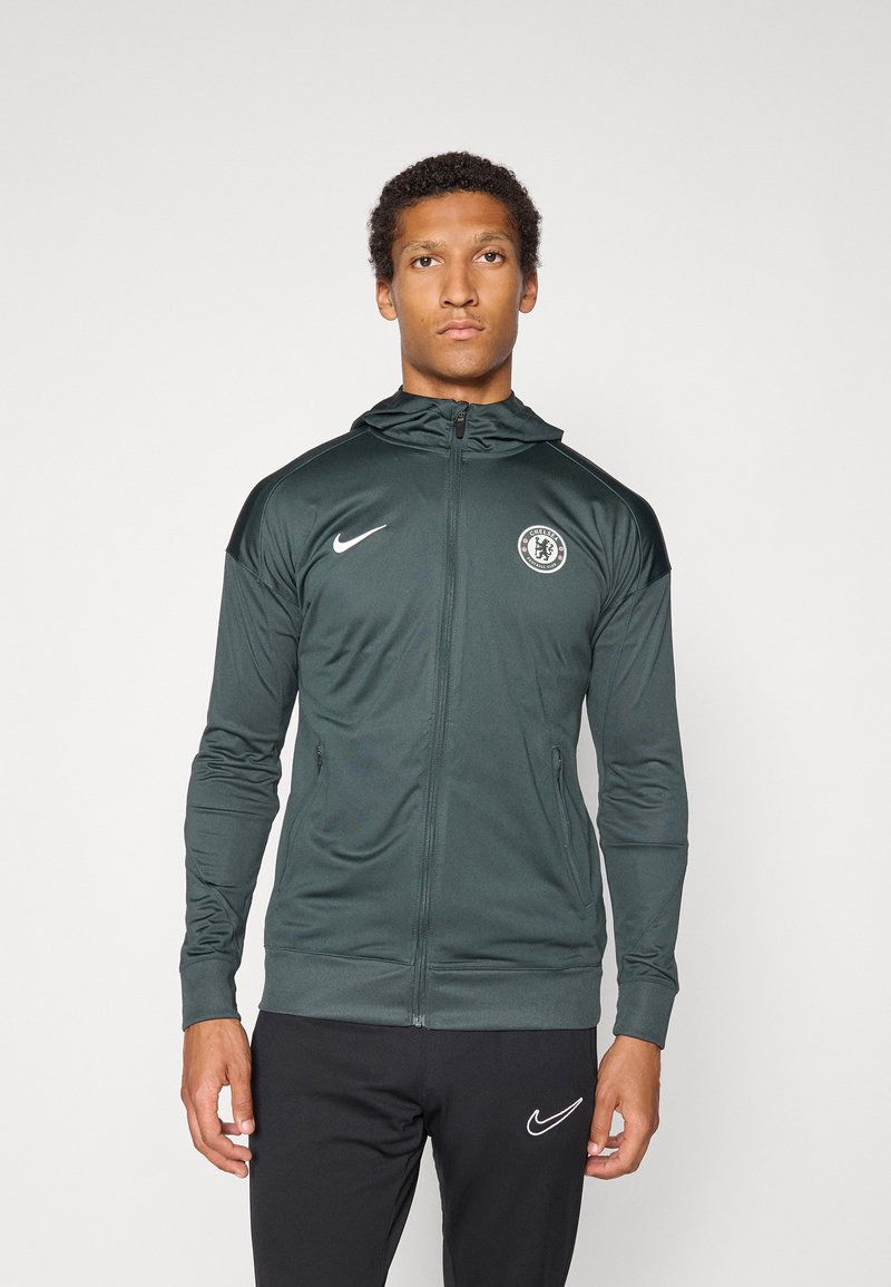 Groene zip-up jasje met capuchon, gemaakt van lichtgewicht stof. Kenmerkt zich door een rond Chelsea FC-logo op de linkerborst en zijzakken.
